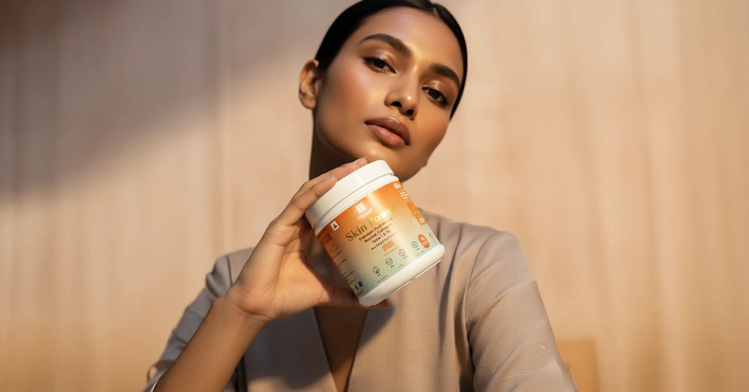 Woman holding ecowell skin power container against a neutral background